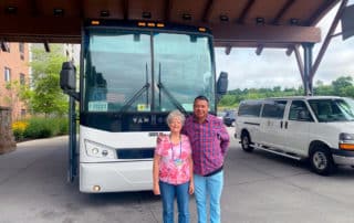 Elder Woman And Man Posing In front OF Tour Bus