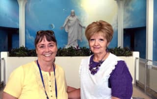 Two Female Visitors Posing In front Of The Christus Statue At The Independence Visitor's Center