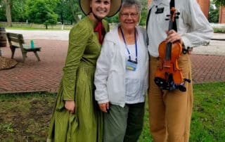 Female Visitor Posing Next To People Wearing Historical Clothing